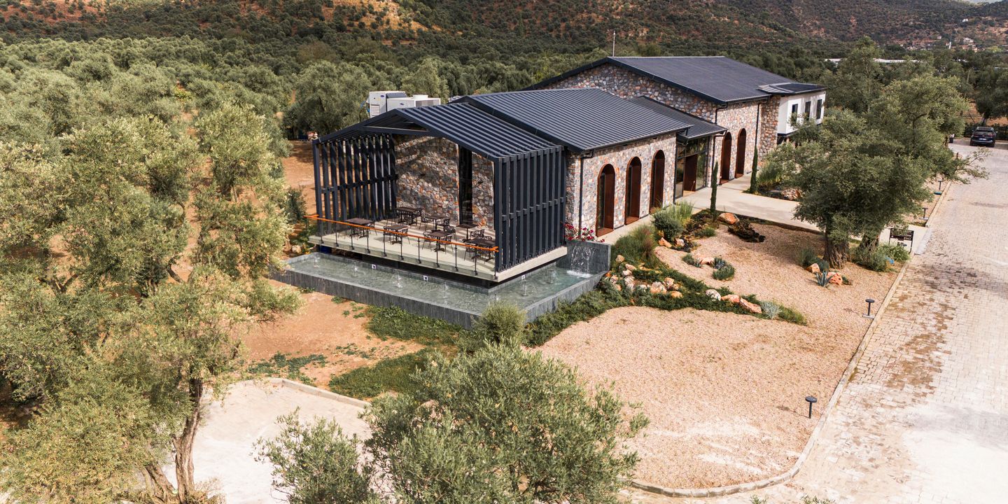 The producer’s stone mill building in Milas, seen from above among olive trees, wooded hills behind